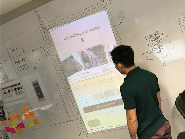 A tester reaching up to the projected full-scale interface on a whiteboard wall, checking reach and ergonomics.