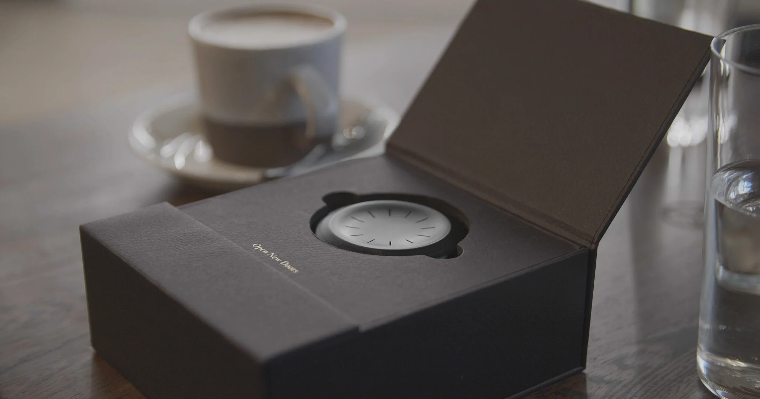 The 'Open New Doors' presentation box open on a café table, the pale smart key seated in a die-cut foam well.